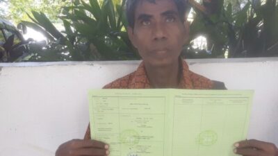 Potret Soleman Matamtasa berdiri di lahan sengketa di Desa Oeteta, Kupang, dengan latar tanaman yang rusak akibat penggusuran.